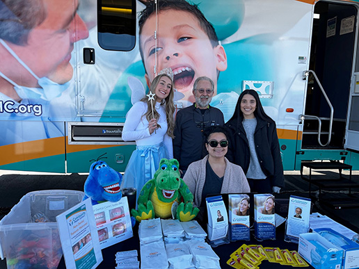 Four people stand behind a booth with dental brochures and supplies.